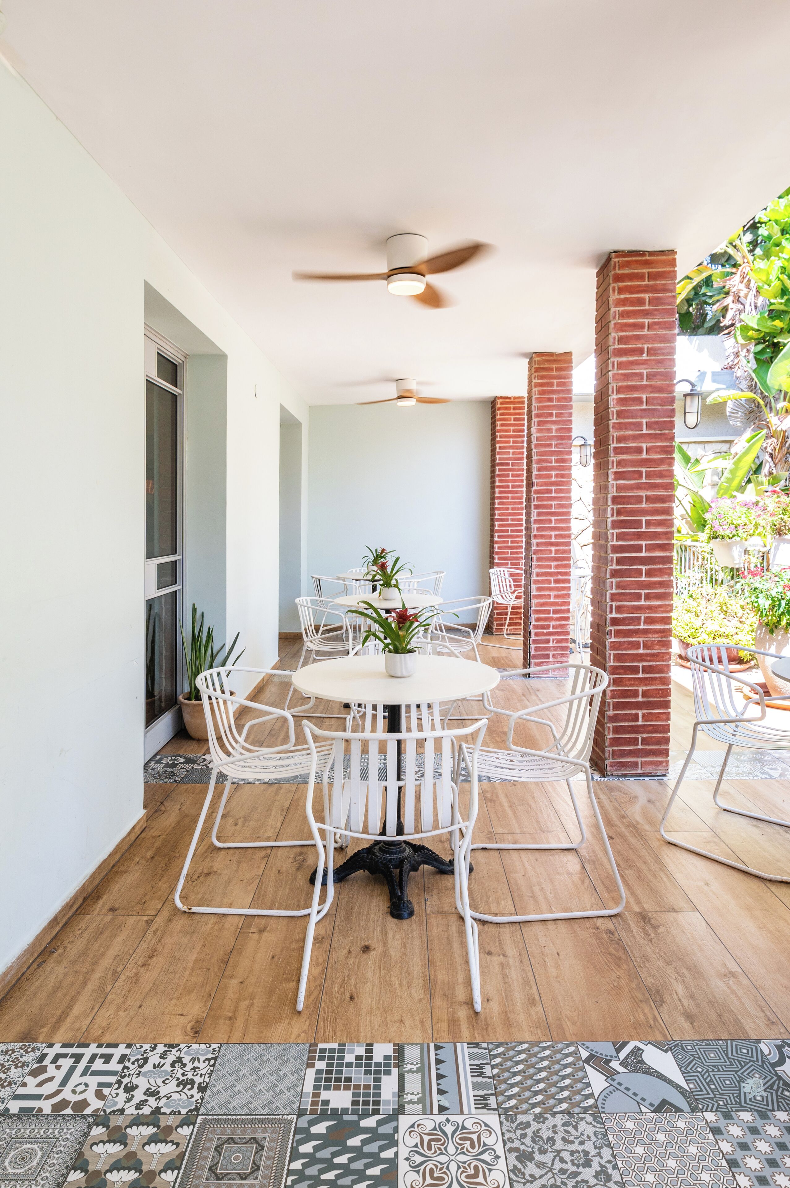 A patio area with a round table and chairs, a ceiling fan, and potted plants.