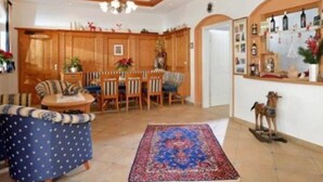 A spacious living room with a large rug, wooden furniture, and a kitchen area in the background. - Holiday (Ellmau)