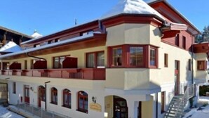 A two-story building with a snow-covered roof, a balcony, and a staircase leading to the entrance. - Holiday (Ellmau)