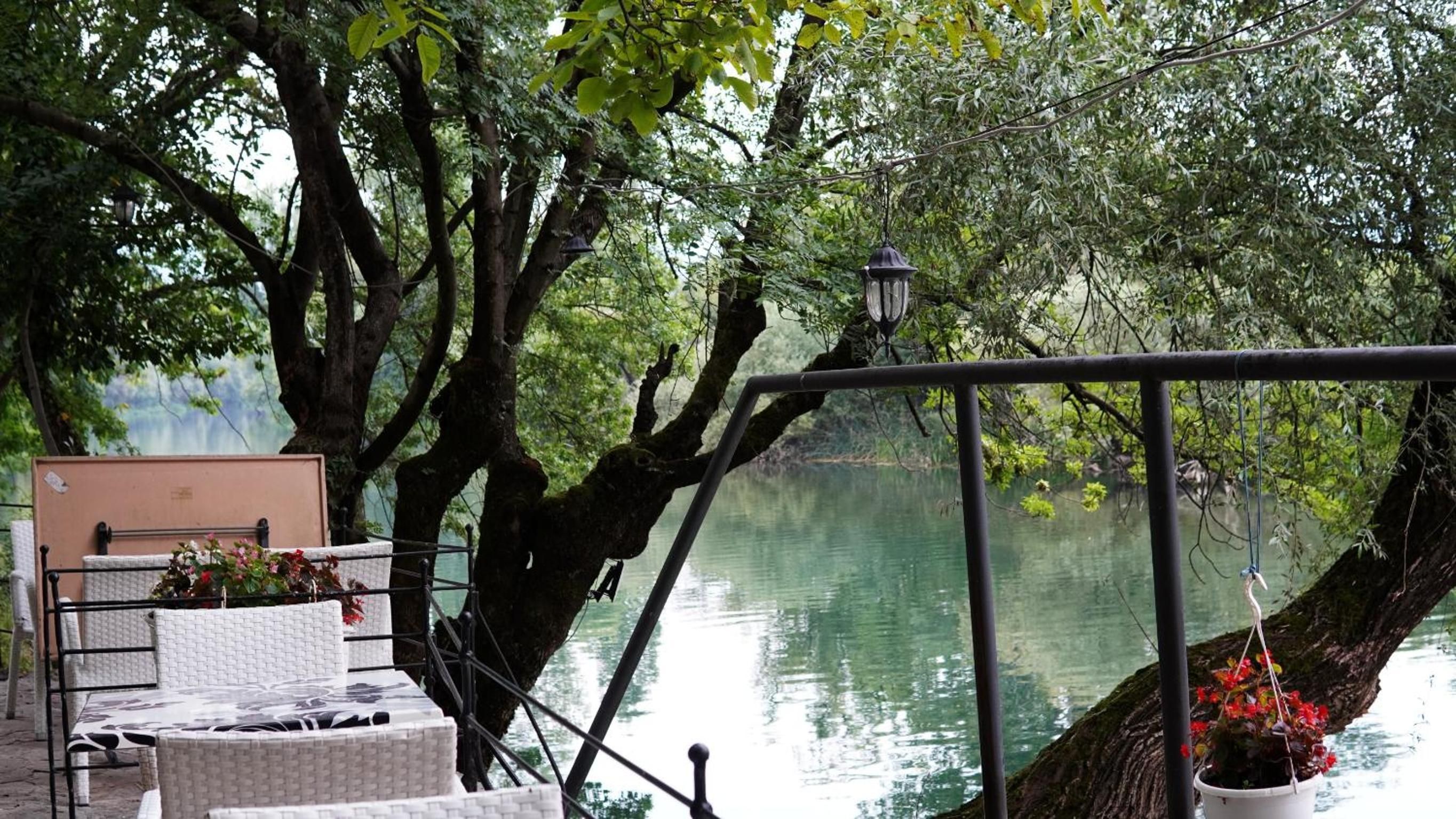 Un espacio tranquilo al aire libre con mesa y sillas, con vistas a un cuerpo de agua en calma, rodeado de exuberante vegetación.