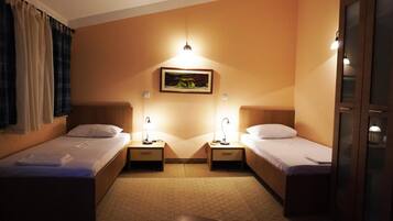 A hotel room with two single beds, bedside tables with lamps, a painting on the wall, and a door on the right.