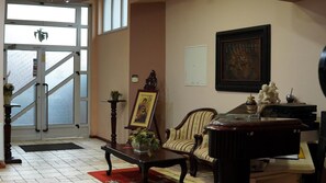 Zona de recepción con escalera, un cuadro enmarcado, una silla, una mesa y una estatua.