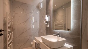 Une salle de bain moderne avec un grand miroir, un lavabo blanc et une douche à parois de verre.