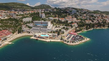 Vista aérea de uma cidade costeira com um hotel em destaque, piscina, estacionamento e praia.