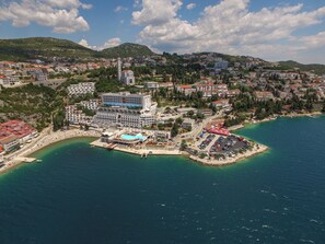 Vista aérea de un pueblo costero con un hotel destacado que cuenta con piscina, zona de estacionamiento y una playa.