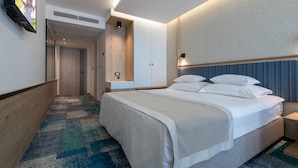 Une chambre d’hôtel moderne avec un grand lit, un téléviseur à écran plat fixé au mur, une table de chevet avec une lampe et une moquette à motifs.