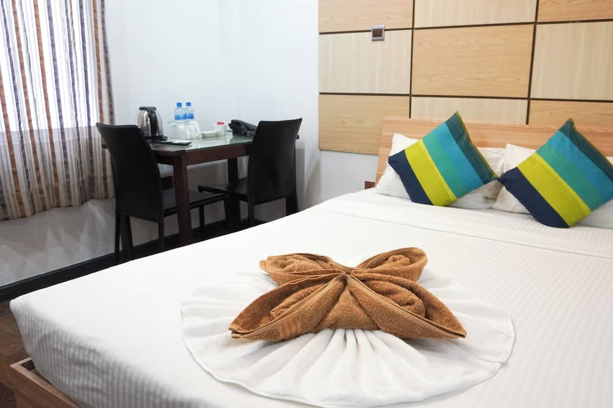 A hotel room with a neatly made bed, a desk with a chair, and a window with curtains.