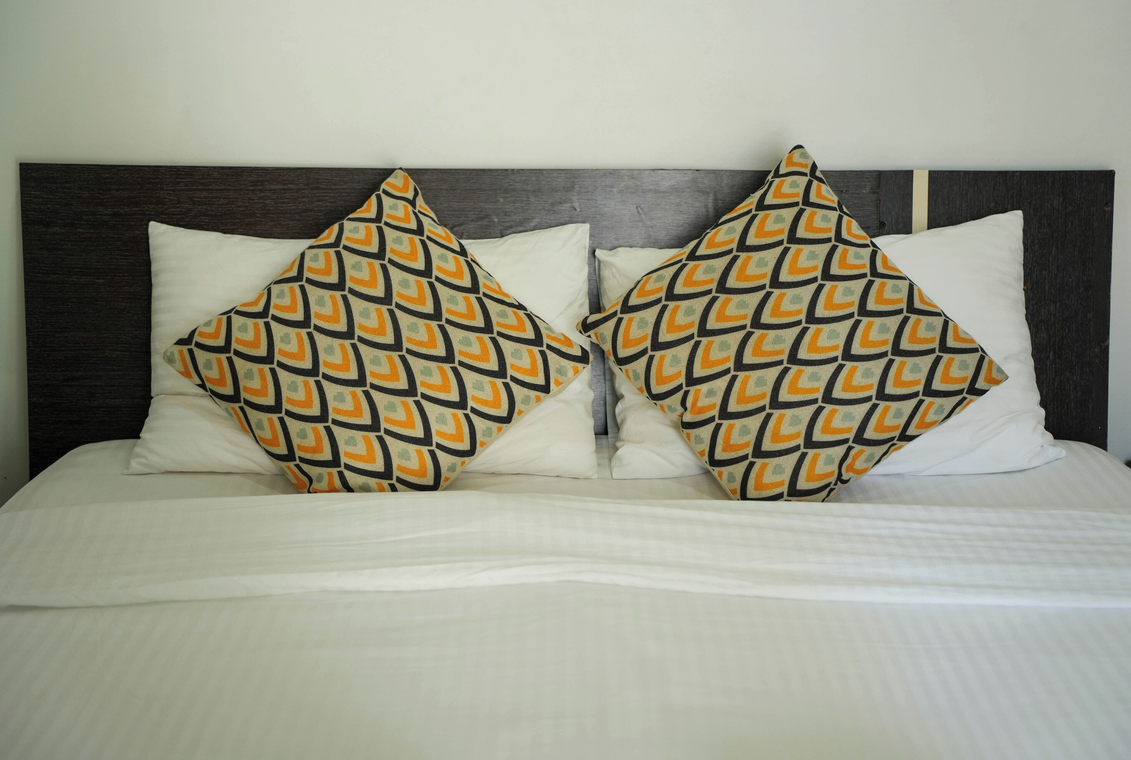 Un lit avec une literie blanche et deux coussins décoratifs à motifs géométriques.