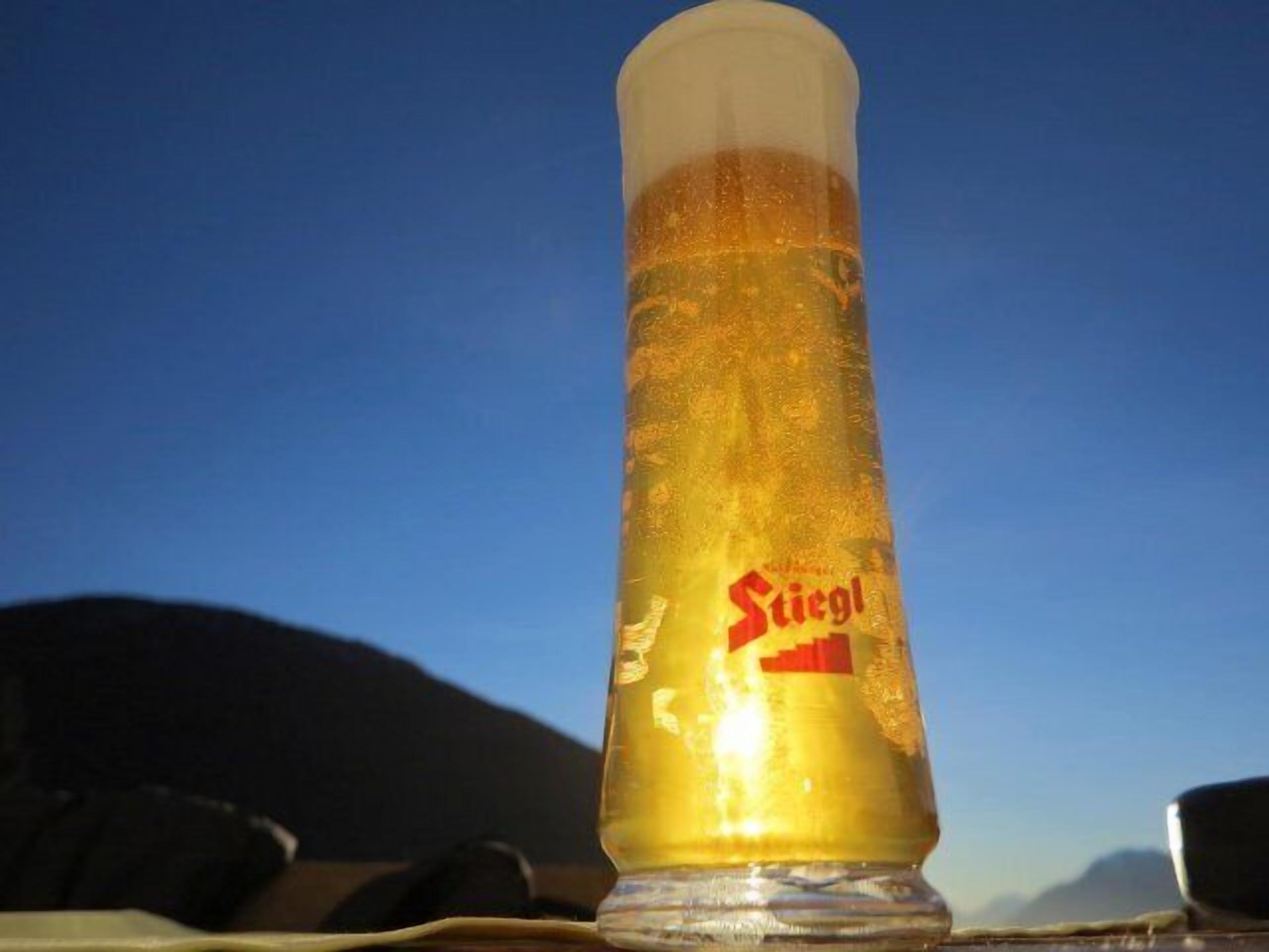 A tall glass with a label reading "Stiegl" against a clear blue sky.