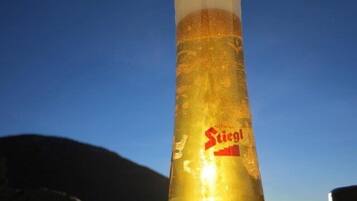 A tall glass with a label reading "Stiegl" against a clear blue sky.