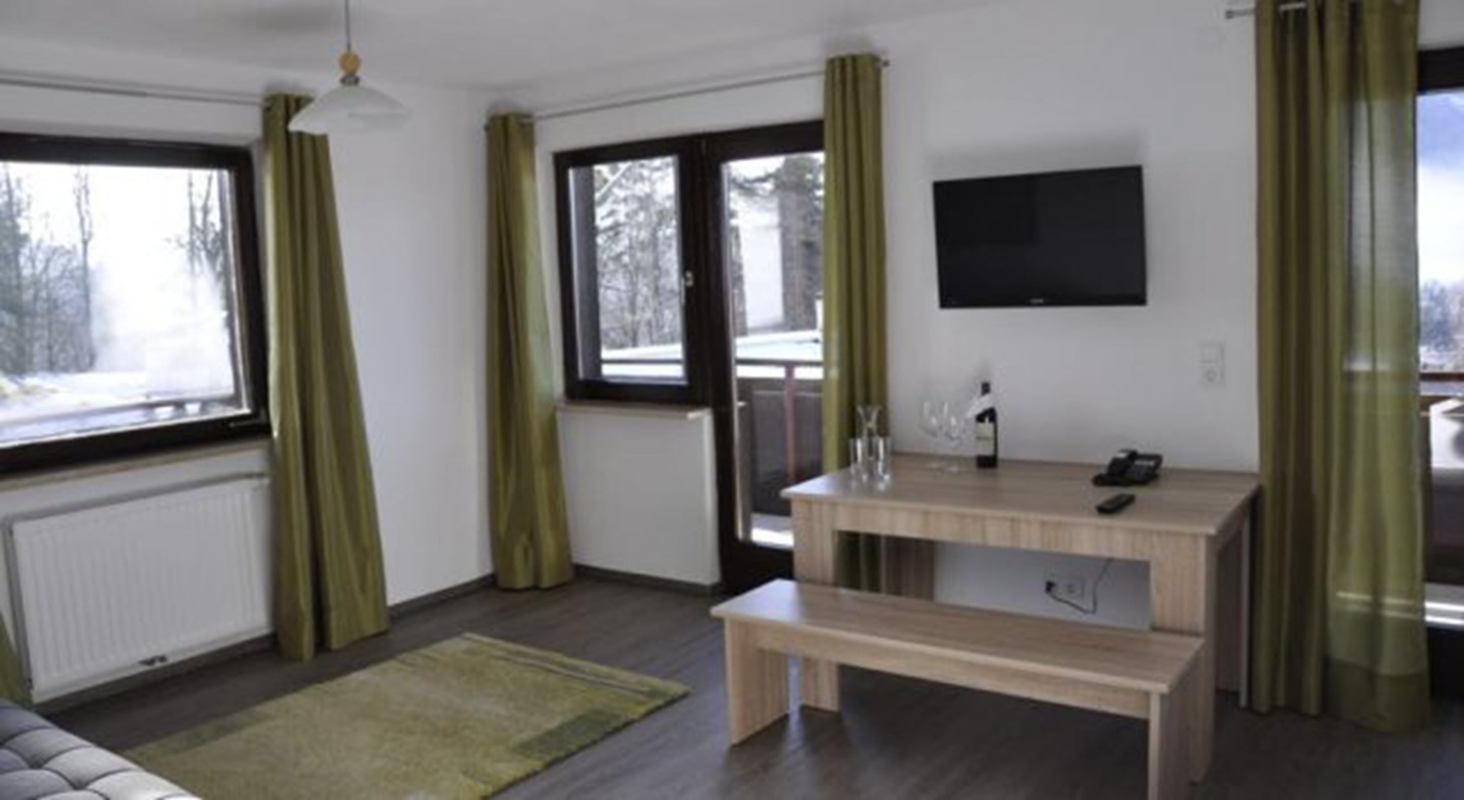 A modern living room with a wooden bench, a TV mounted on the wall, and a window with curtains.