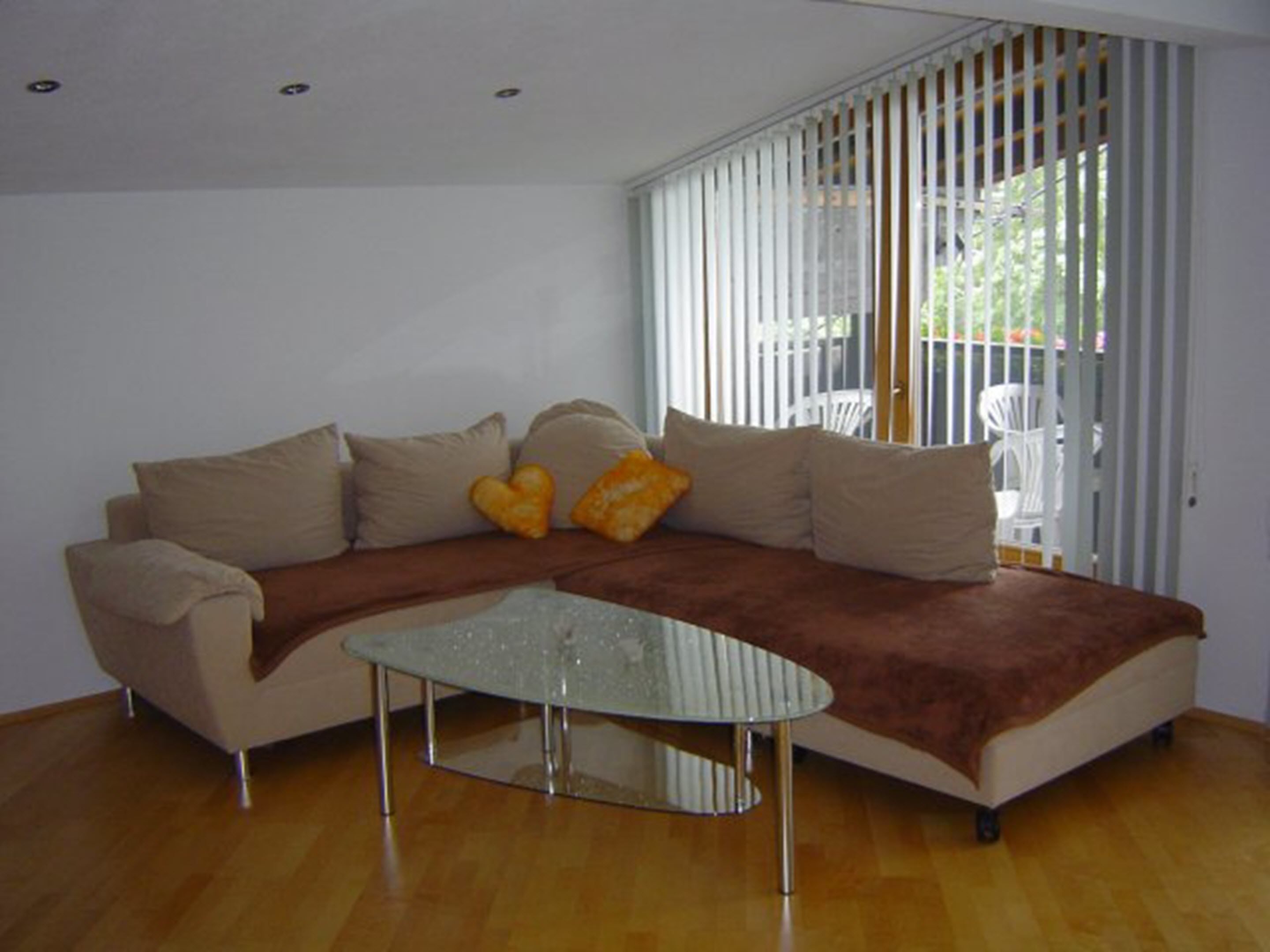 A living room with a sofa, a glass coffee table, and a view through a window with blinds.