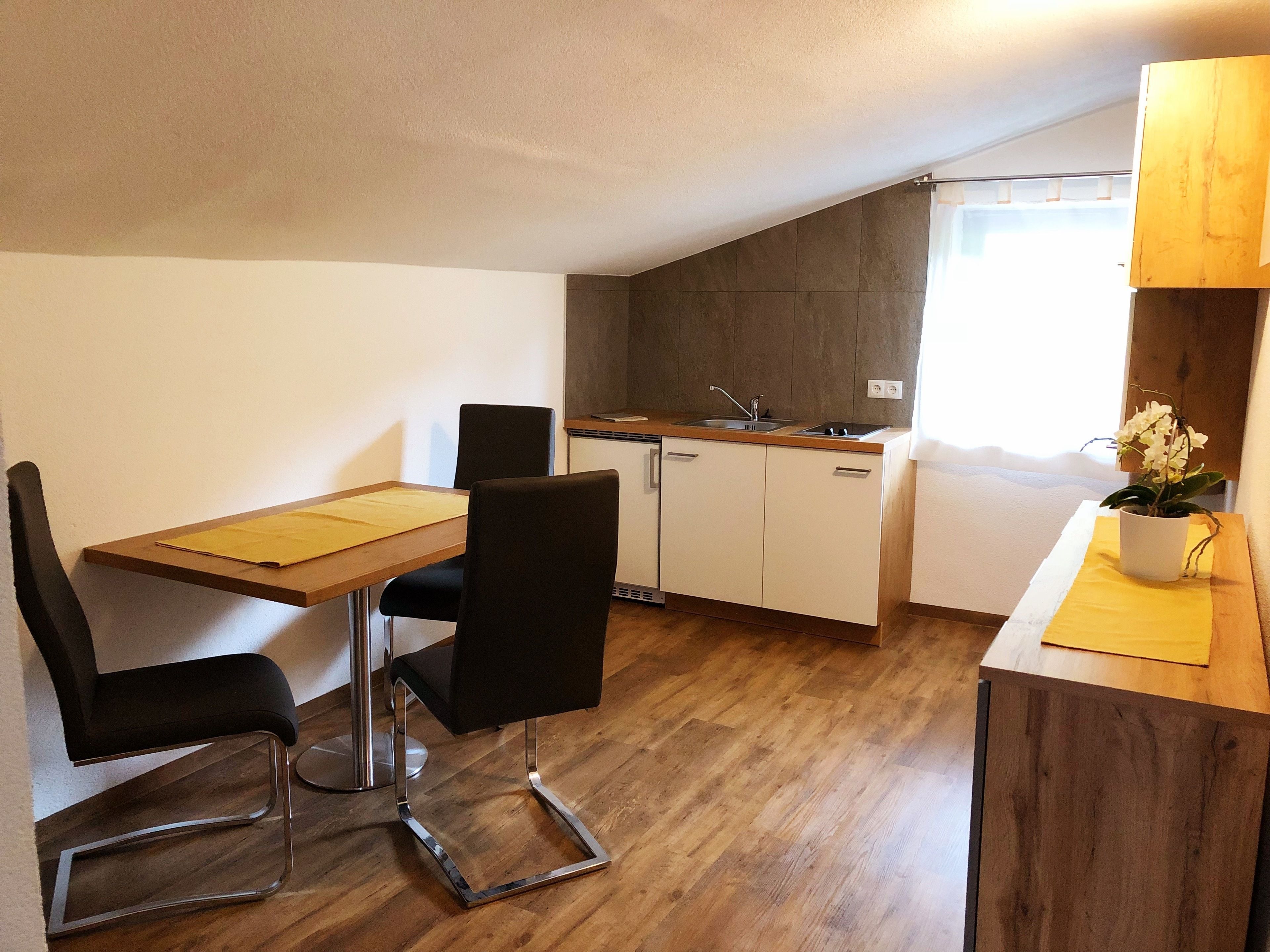Una cocina compacta con una mesa y sillas de madera, un lavamanos y una orquídea en maceta.
