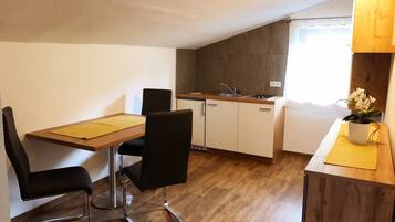 A compact kitchen with a wooden table and chairs, a sink, and a potted orchid.