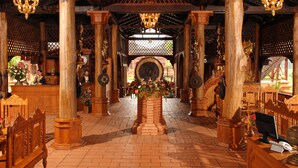 Een ruime binnenruimte met hoge houten zuilen, een centraal bloemarrangement en een kroonluchter.