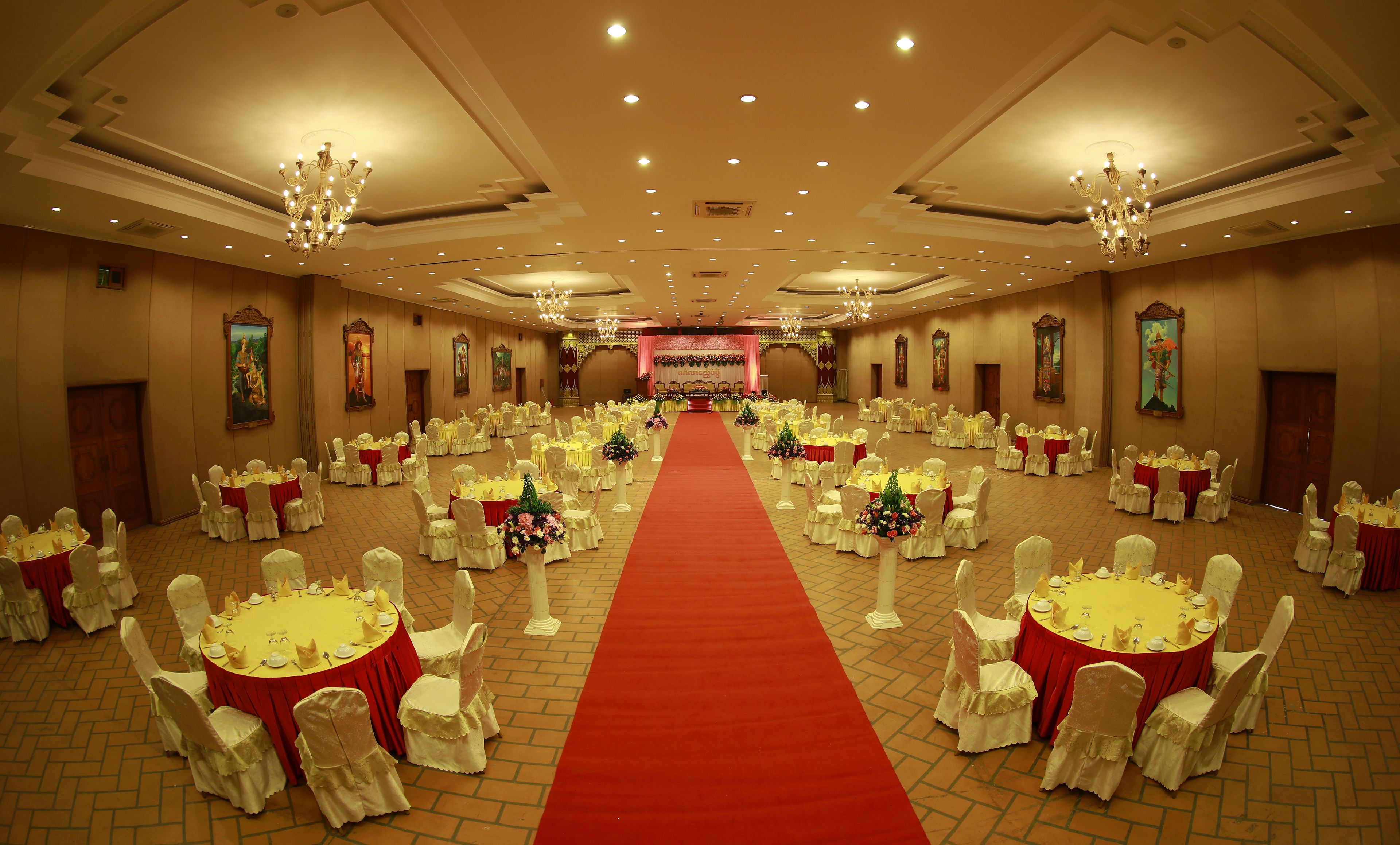 A banquet hall with round tables, red carpets, and chandeliers.