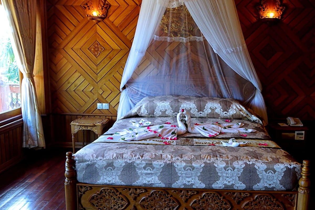 Een bed met hemelbed, een versierd houten hoofdbord en bloemenbeddengoed.