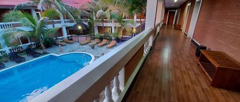 A hotel with a swimming pool, lounge chairs, and a covered outdoor seating area.