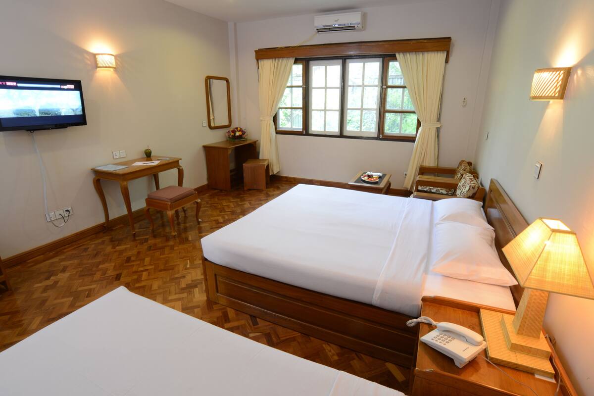 Ein Hotelzimmer mit einem hölzernen Bett, einem Schreibtisch, einem Stuhl, einem Fernseher und einem Fenster mit Vorhängen.