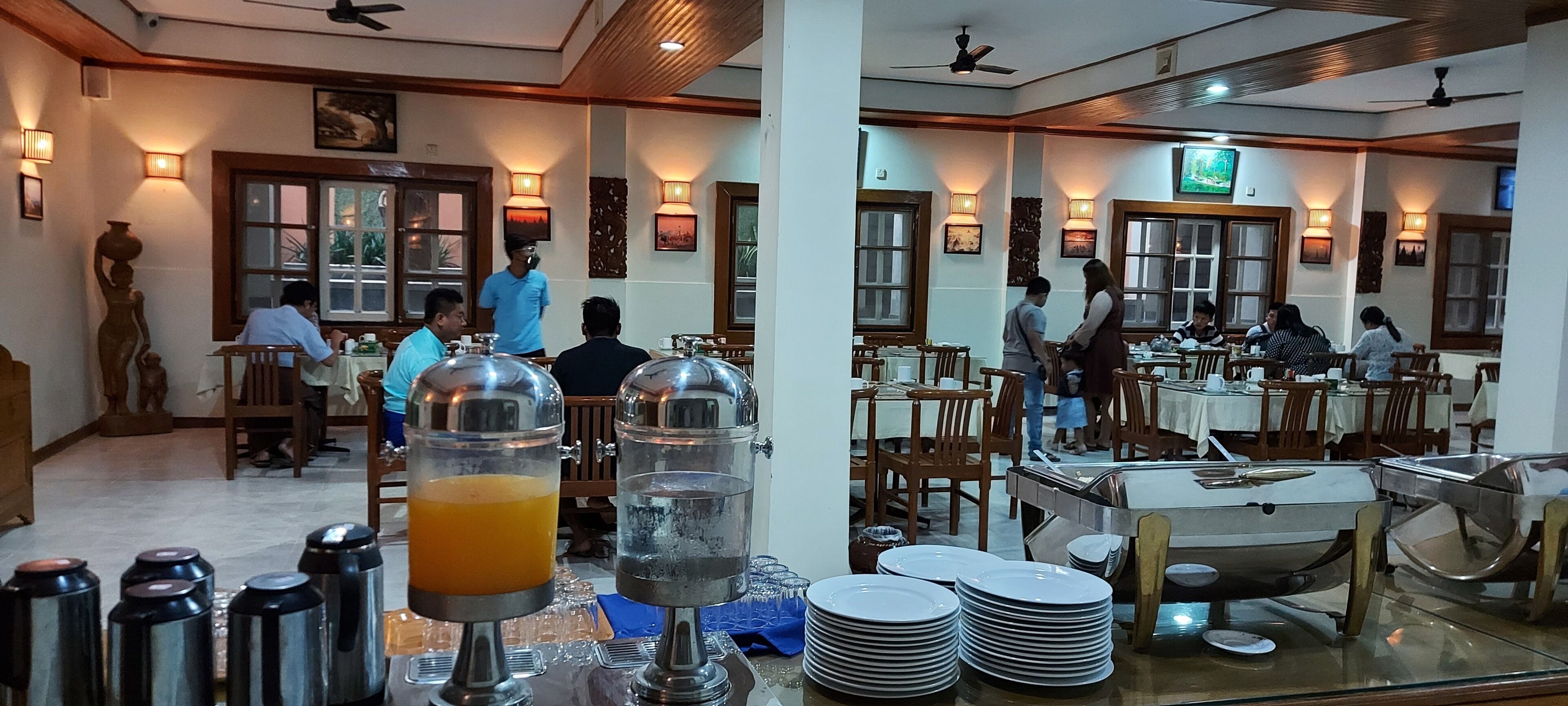 A restaurant with wooden furniture, tables, and chairs, and a buffet area with food and drink containers.
