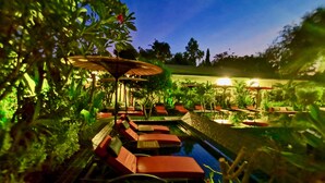 Un jardín tranquilo con un estanque pequeño, sillones de relax rojos y sombrillas.