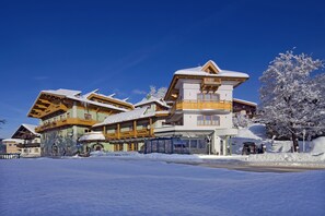 A multi-story hotel with a snow-covered roof and wooden balconies, surrounded by snow. - Hotel Obermair (Fieberbrunn)