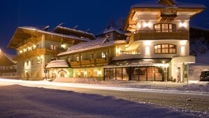 A multi-story hotel with a snow-covered roof, large windows, and a balcony. - Hotel Obermair (Fieberbrunn)