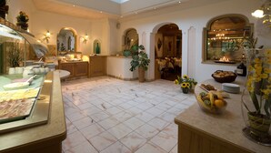 A spacious hotel lobby with a high ceiling, a marble floor, and a central seating area with a buffet. - Hotel Obermair (Fieberbrunn)