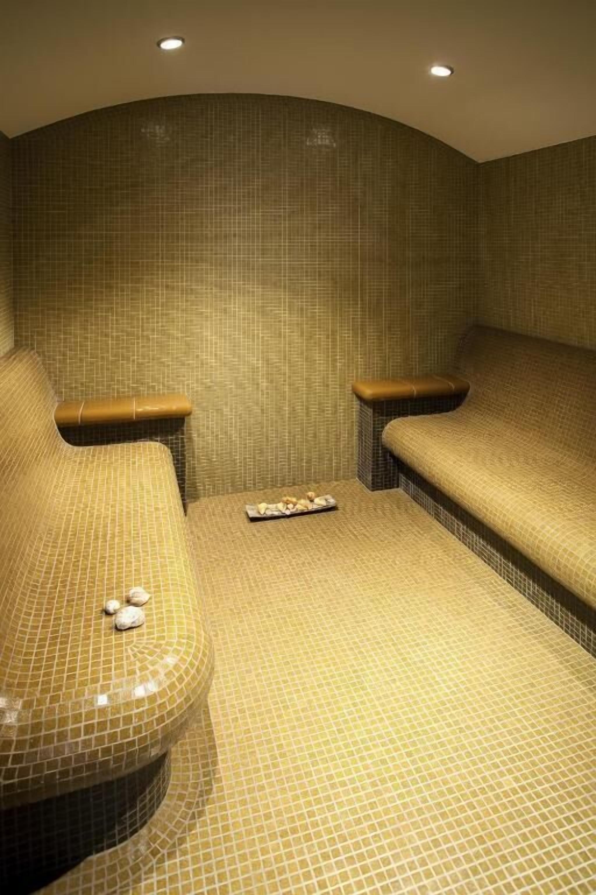 Un cuarto de spa con dos camillas de masaje, una bandeja pequeña con velas y una pared de azulejos.