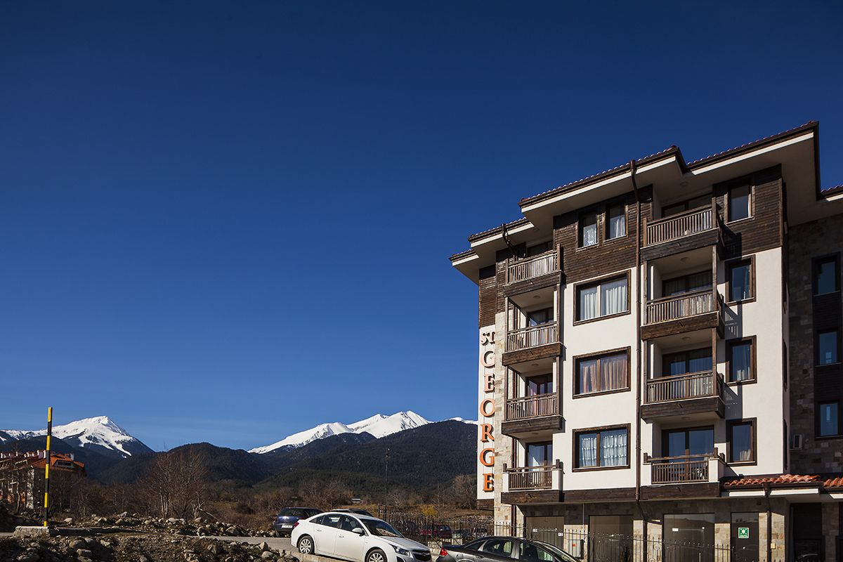 A multi-story hotel with balconies and a view of snow-capped mountains in the background.