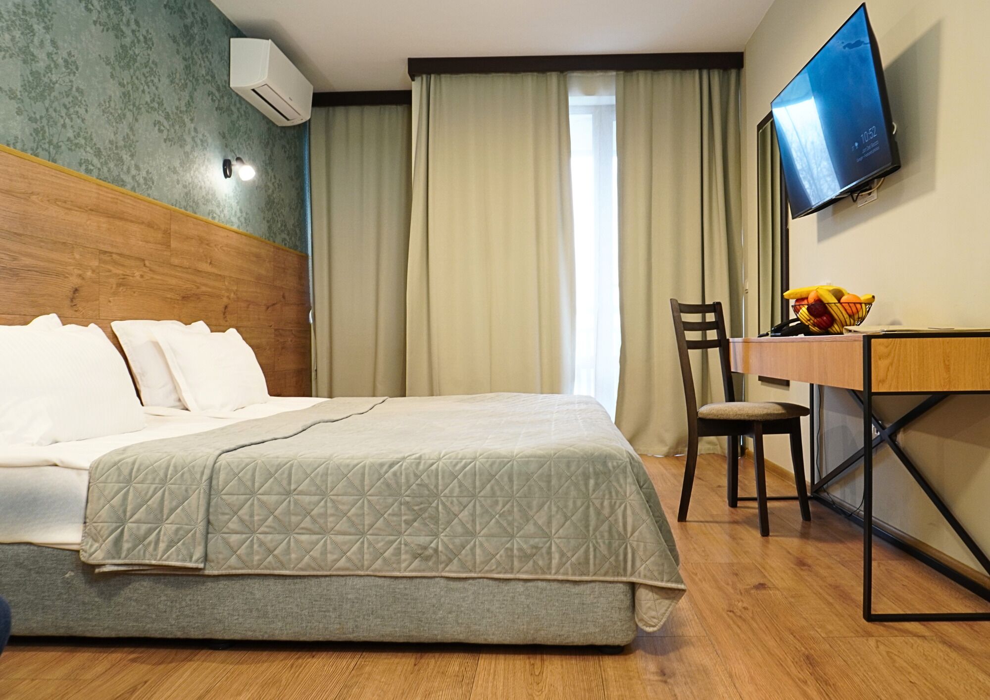 A hotel room with a bed, a desk with a chair, a television, and a window with curtains.