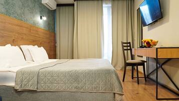 A hotel room with a bed, a desk with a chair, a television, and a window with curtains.