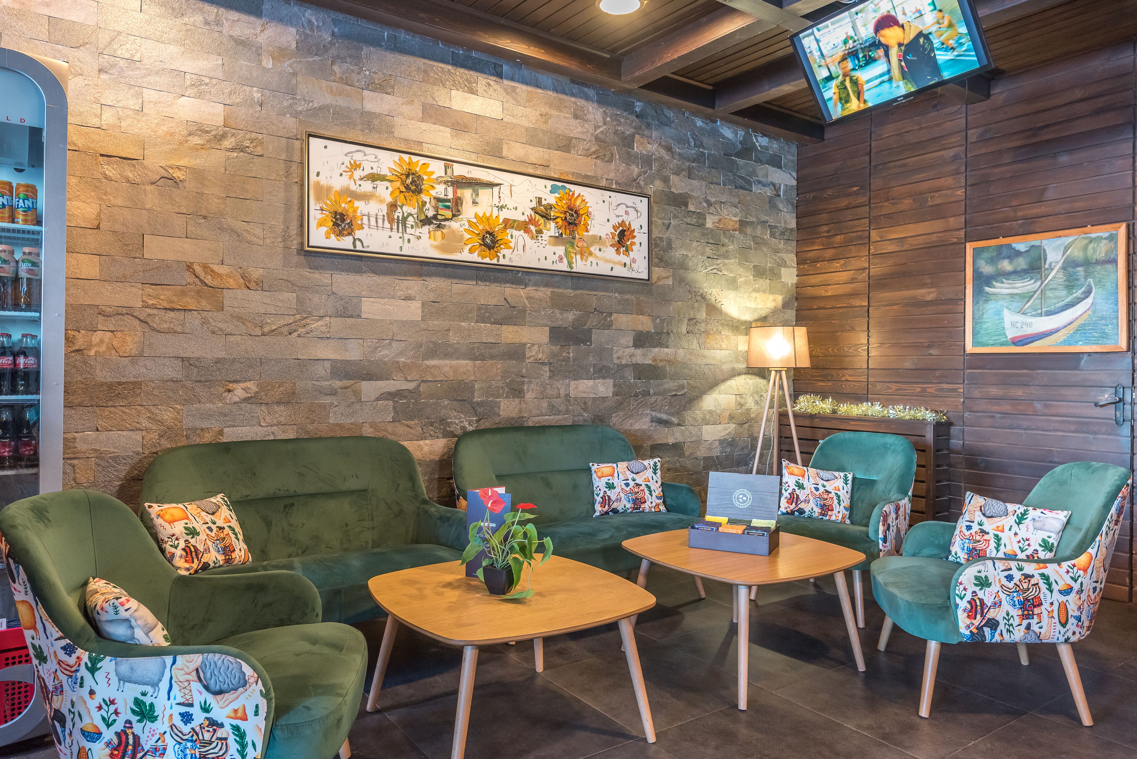 A cozy lounge area with green sofas and armchairs, a wooden coffee table, and a TV mounted on the wall.