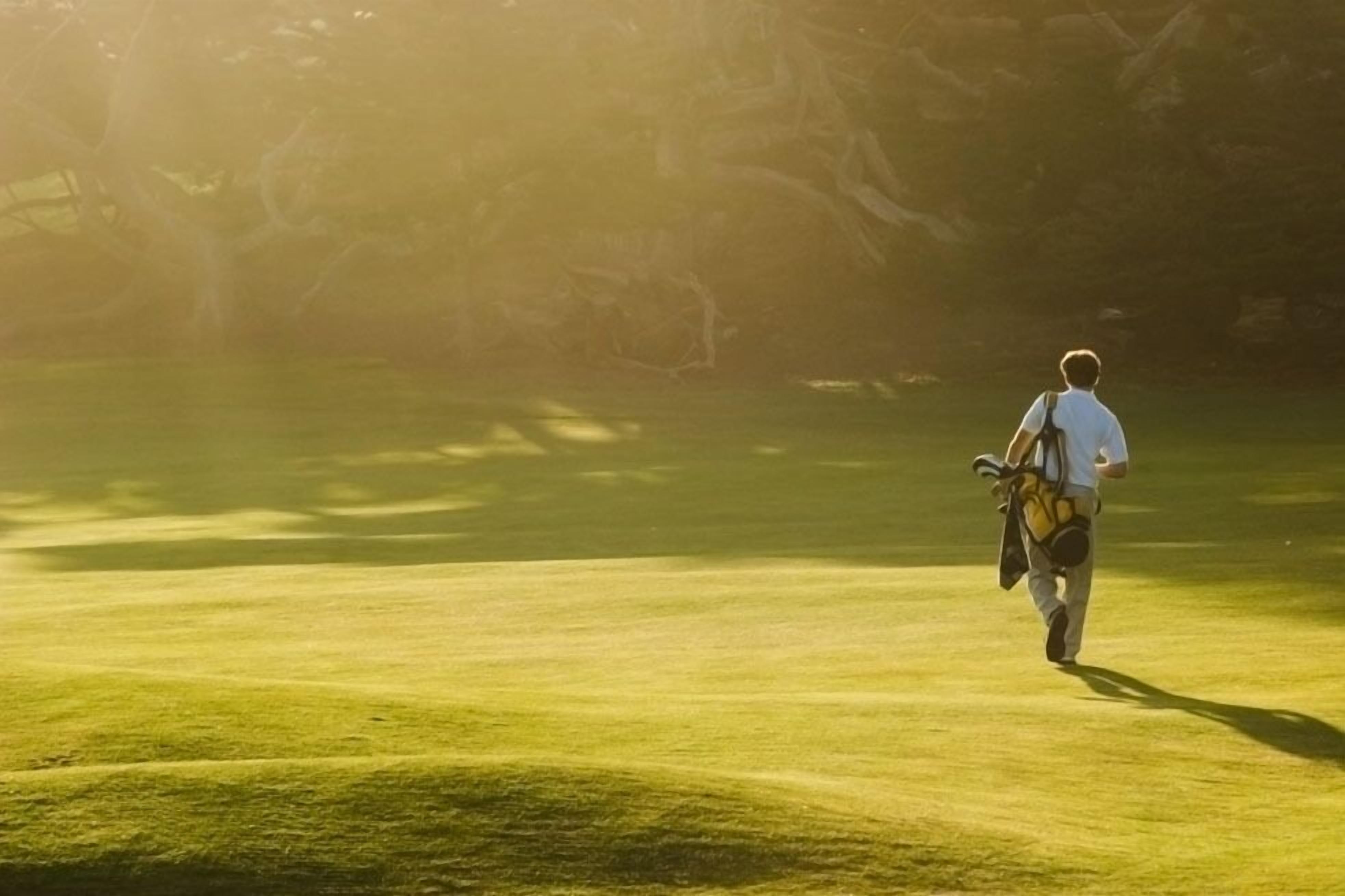 A person walking on a golf course with a bag.