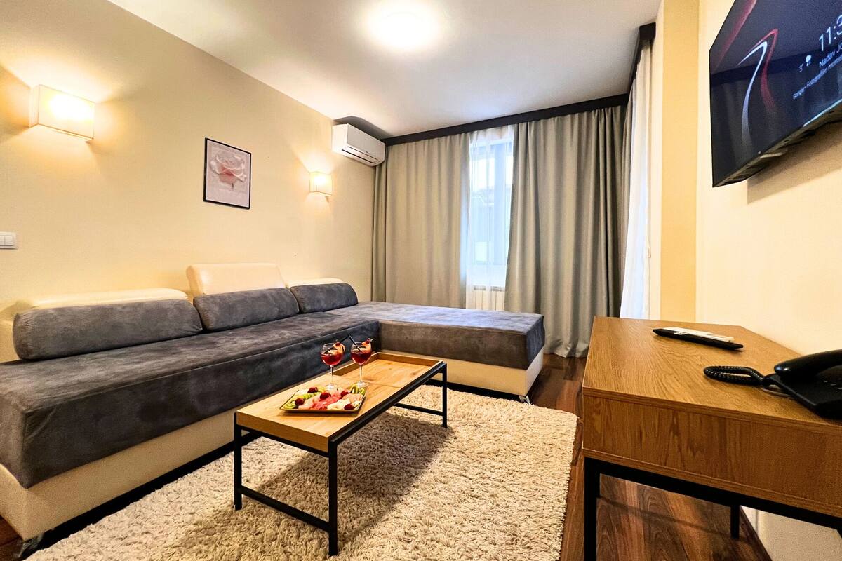 A modern living room with a sofa, a coffee table with fruit, a TV, and a desk with a phone.