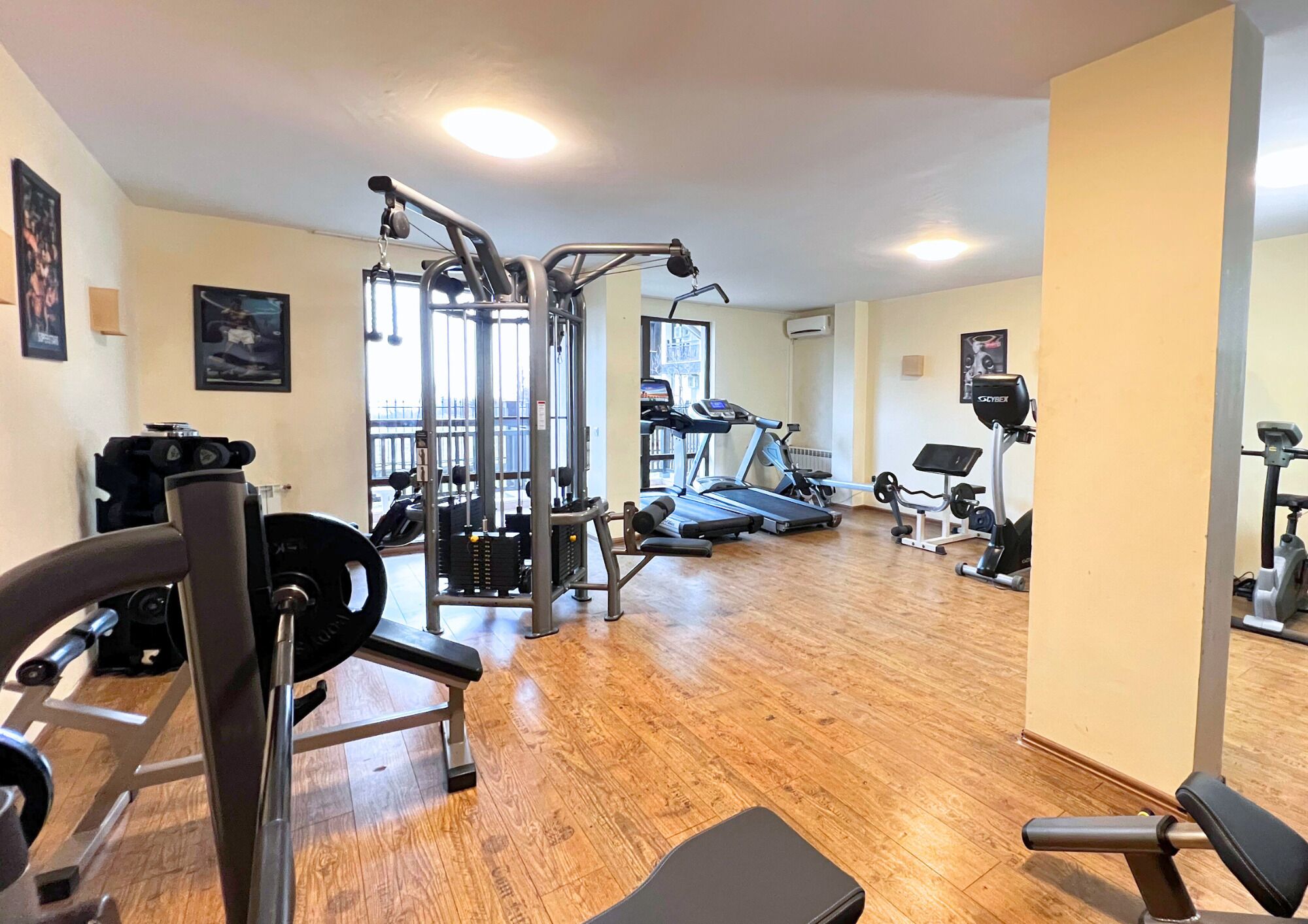 A gym with various exercise equipment, wooden flooring, and a view of the outdoors.