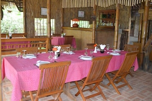 A dining area with a table set for four, surrounded by wooden chairs, and a bamboo wall structure.