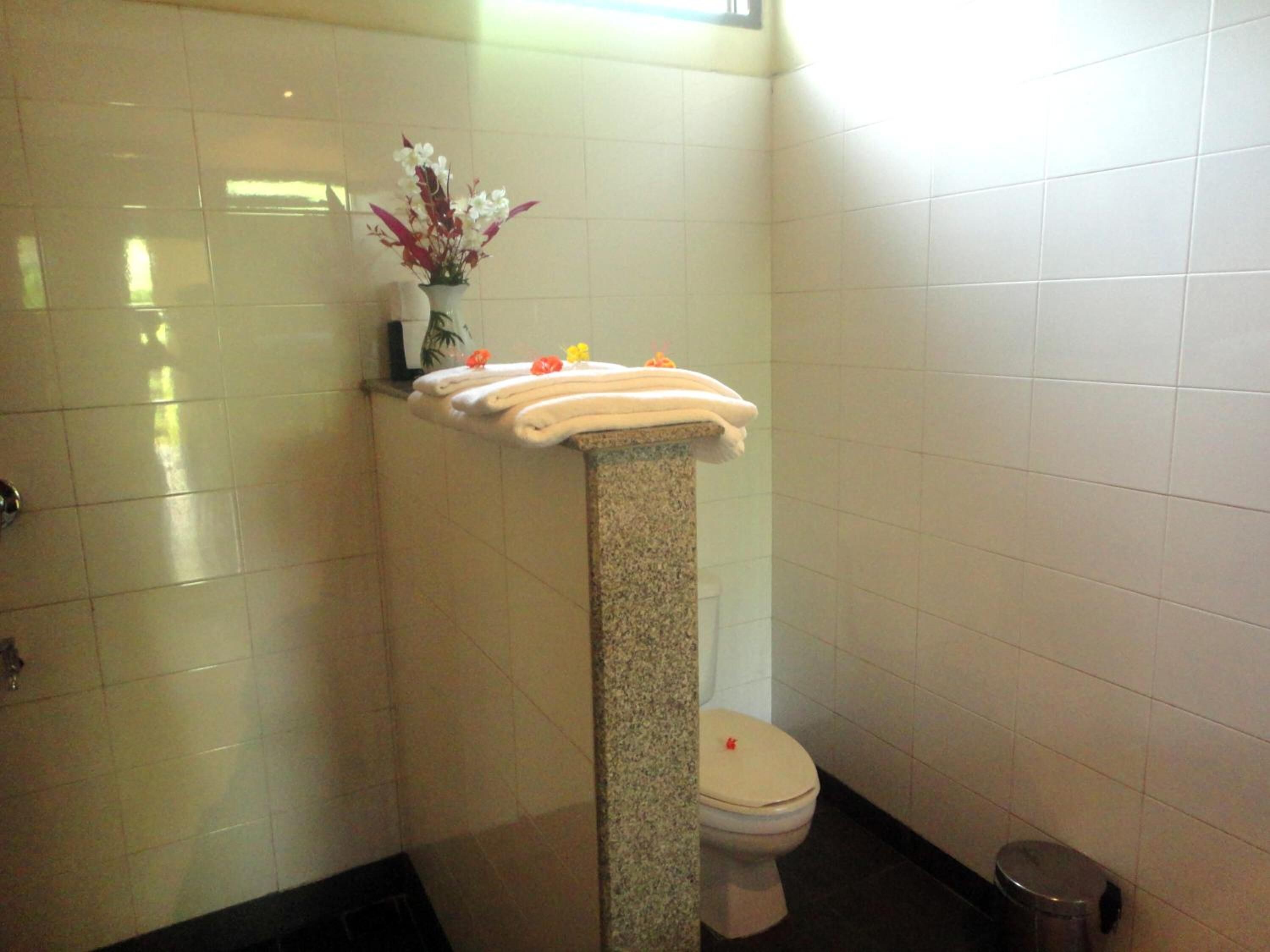Baño con paredes de azulejos blancos, lavamanos de granito sobre pedestal, inodoro y un cubo de basura.