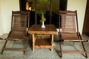 A wooden table with a woven tabletop and two wooden chairs with slatted backs. A white vase with flowers is placed on the table. - Golden Sunrise Hotel (Kyaikto)