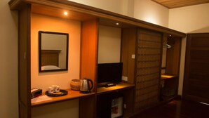 Una habitación de hotel con una mesa consola de madera, un televisor, un refrigerador pequeño y una puerta corredera.