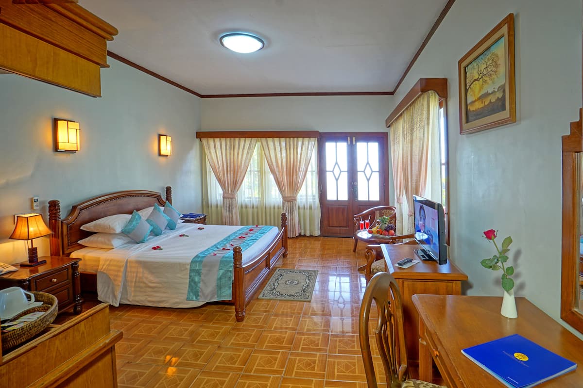 Ein Hotelzimmer mit Bett, Nachttisch, Lampe, Fernseher und Schreibtisch mit Blumen in einer Vase.