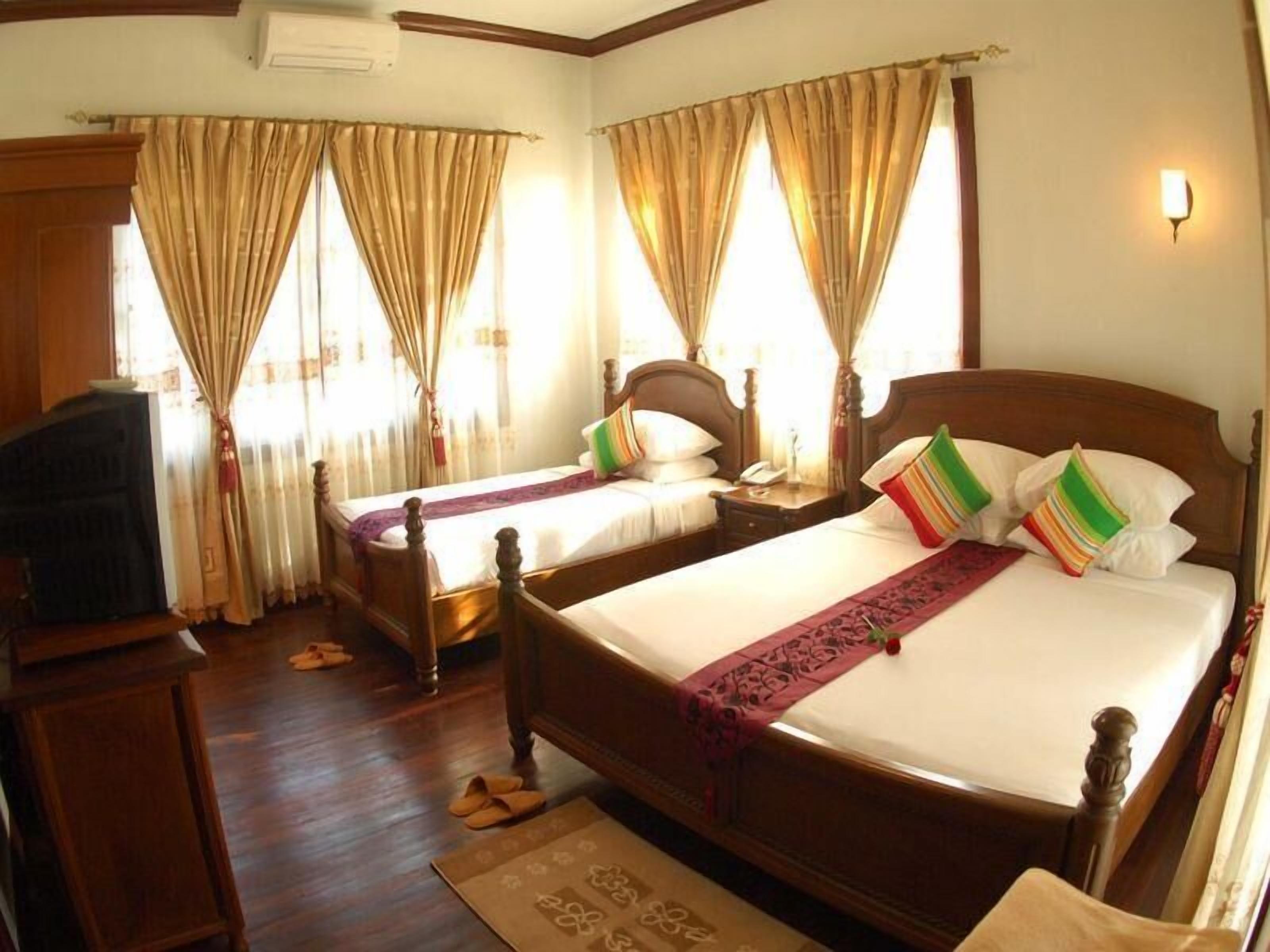 A hotel room with two wooden beds, a wooden wardrobe, and a television.
