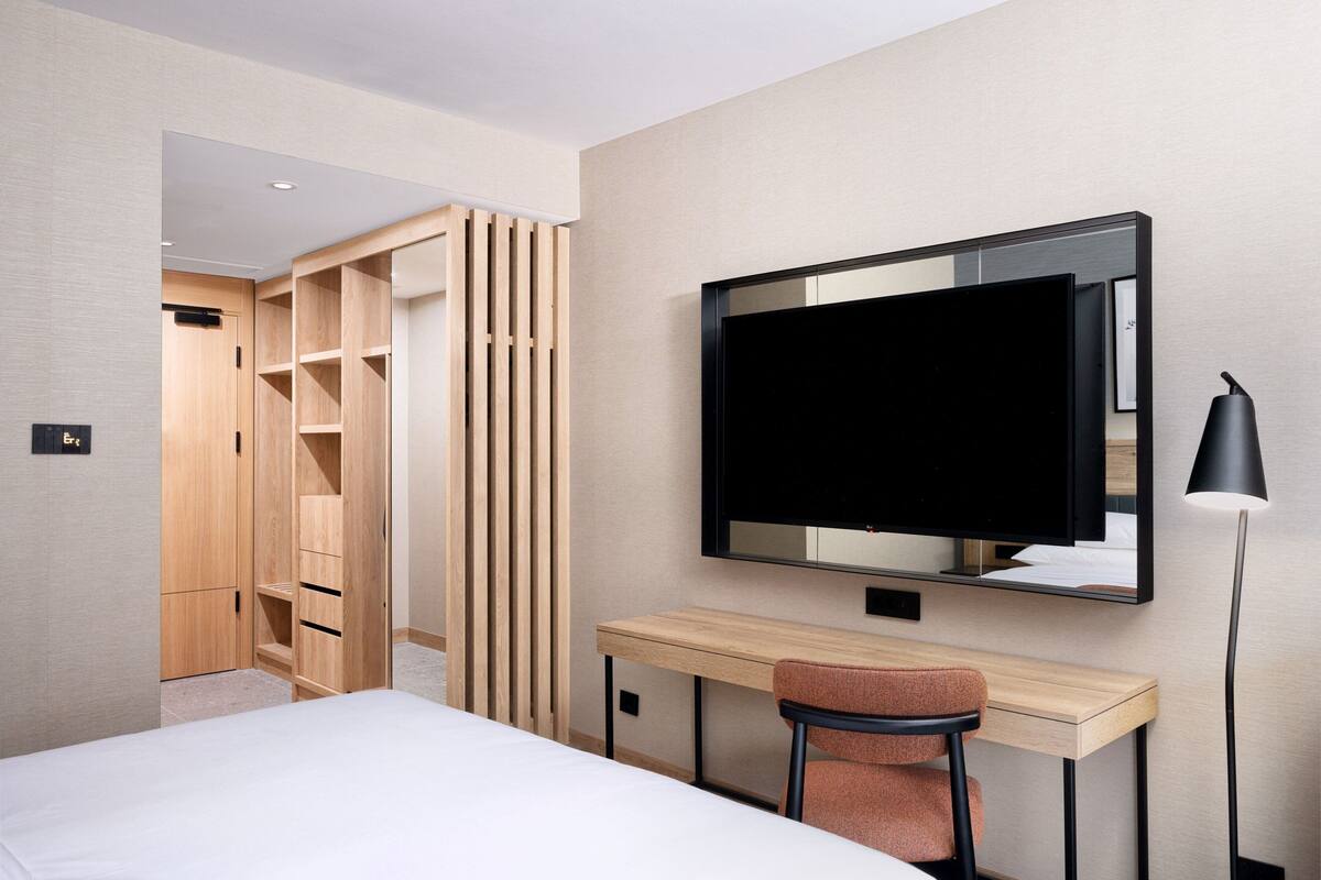A hotel room with a bed, a desk, a chair, a TV, and a wardrobe.