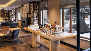 A modern dining area with a long wooden table set for a buffet, a stone fireplace, and a cozy seating area with a sofa and chairs. - Four Points by Sheraton Bansko (Bansko)