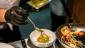 A chef preparing a dish with a spoon, a bowl, and a pan on a stainless steel table.