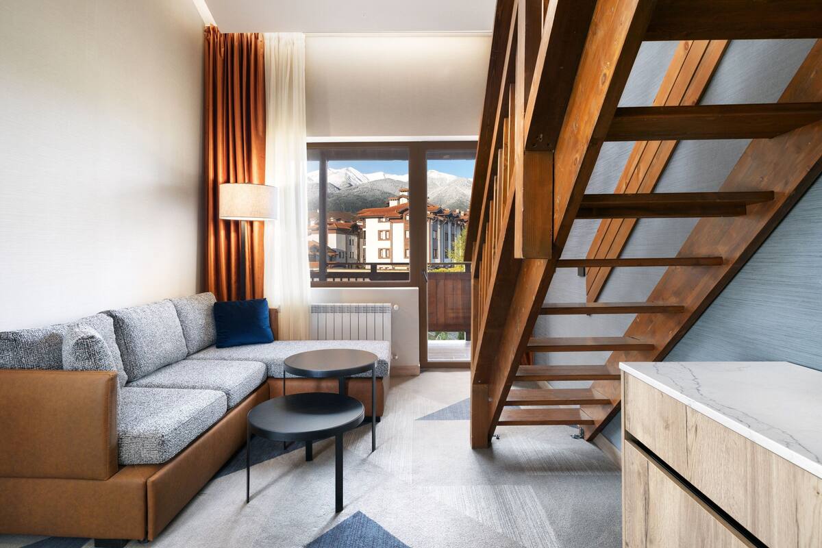 A modern living room with a sofa, a small round table, and a wooden staircase.