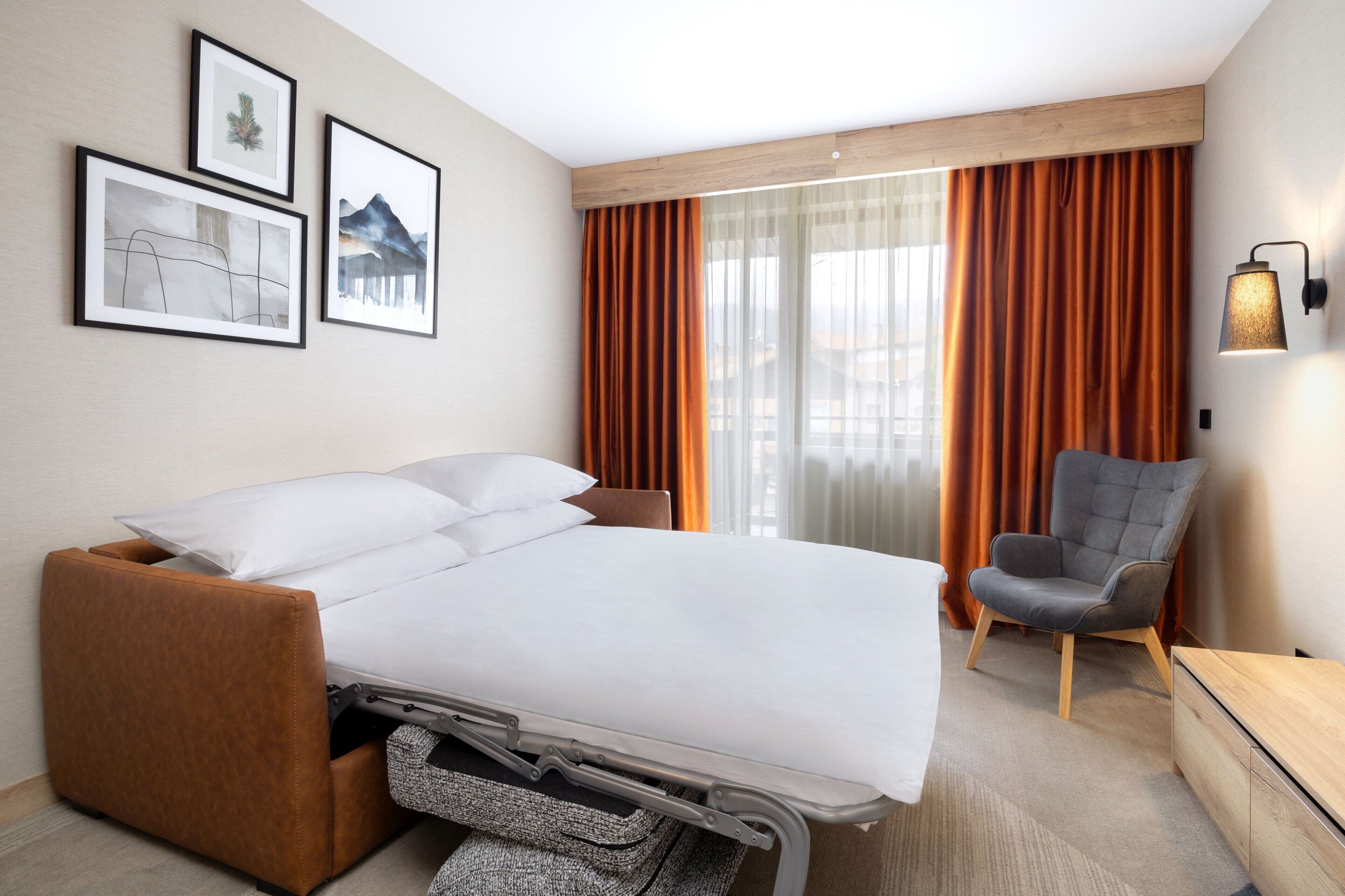 Una habitación de hotel moderna con una cama, una silla y obras de arte en la pared.