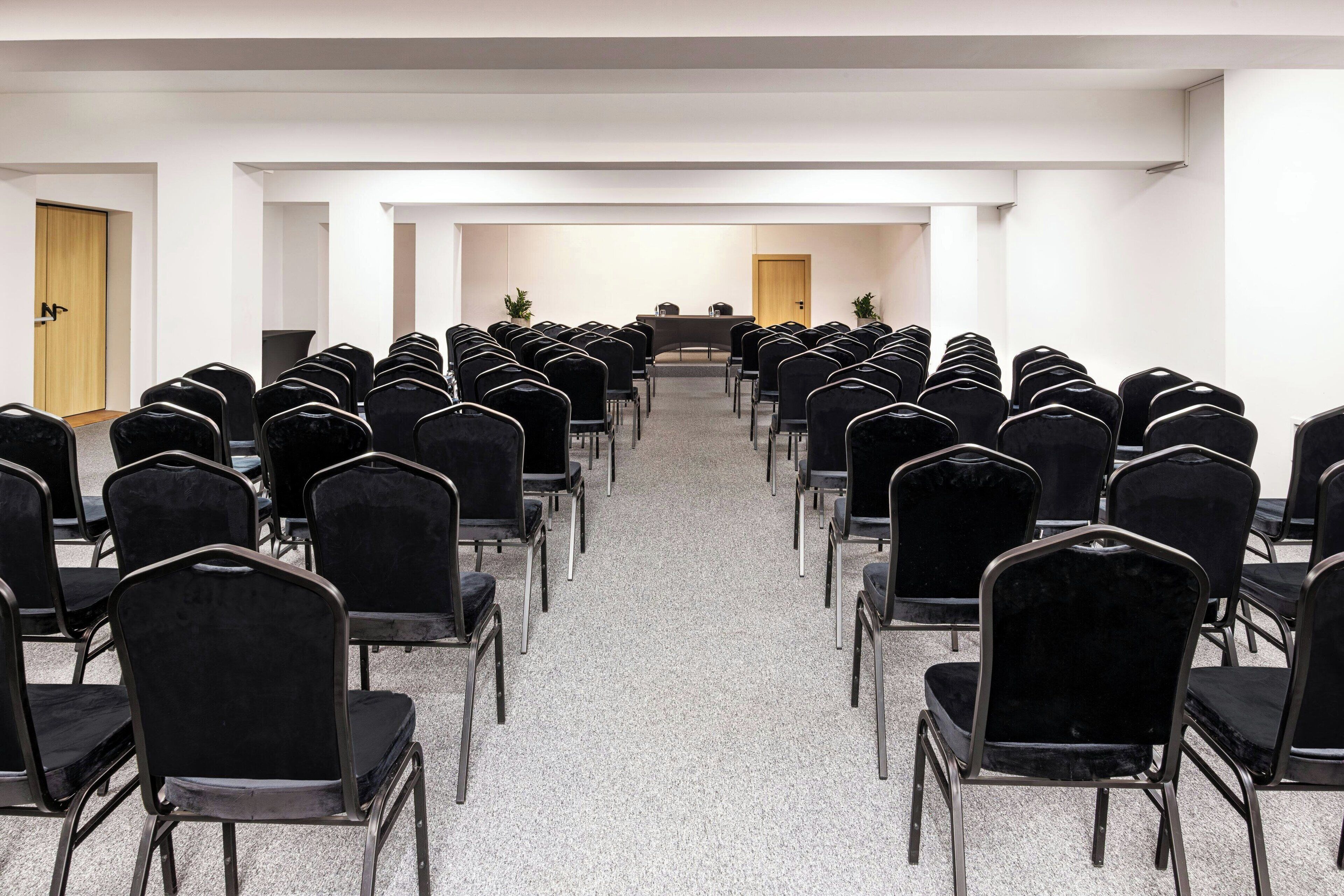 A conference room with rows of black chairs facing a long table at the front.