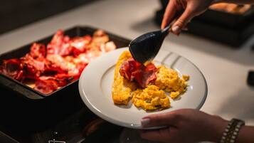 Una persona sirve huevos revueltos y tocino en un plato.