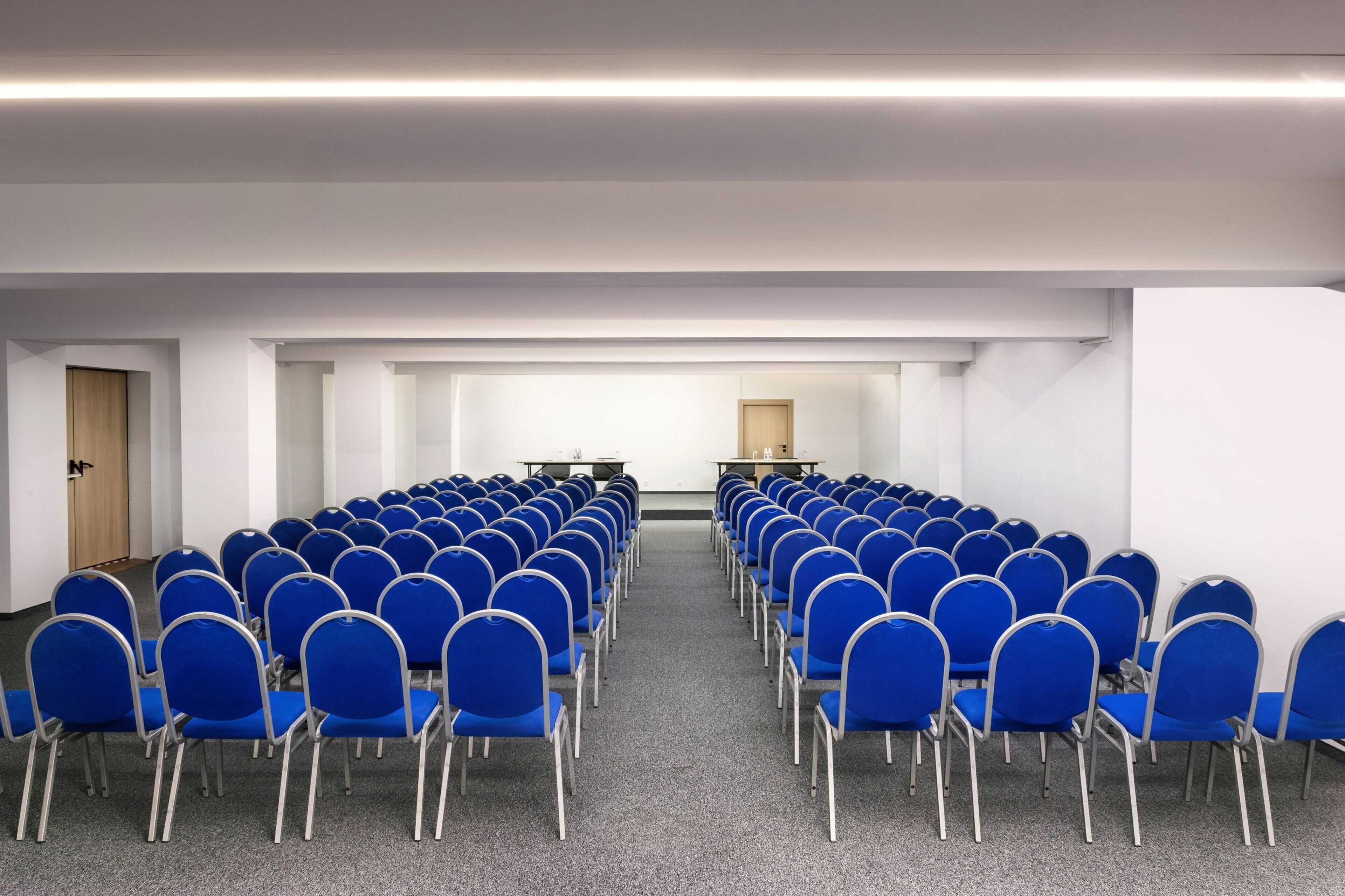 Un salón de conferencias con filas de sillas azules y un atril al frente.